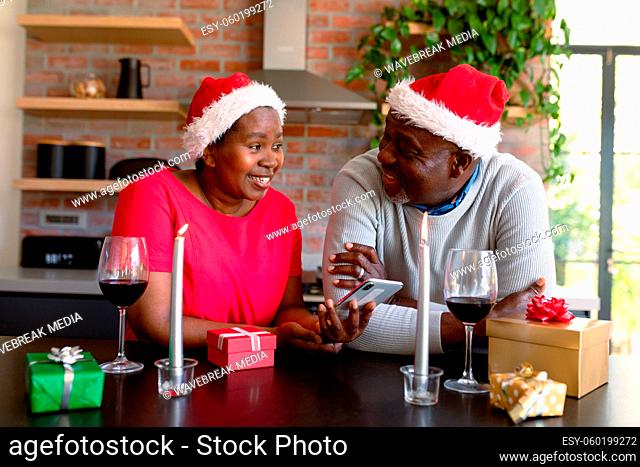 Happy african american senior couple in santa hats using smartphone in kitchen at christmas time