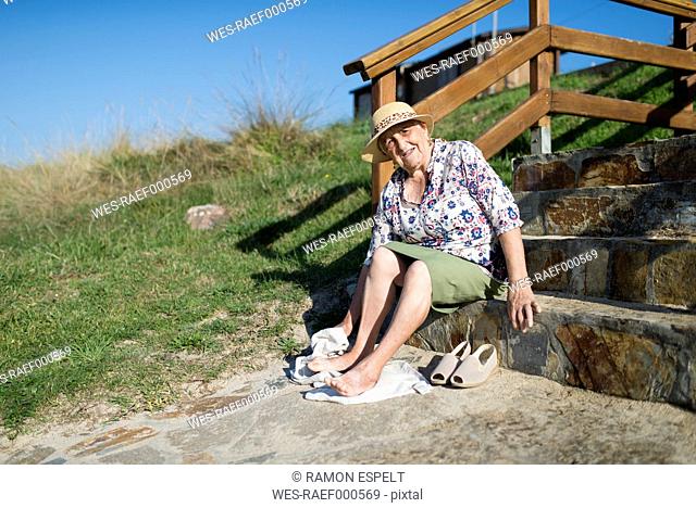 Senior woman sitting on stairs wiping sand off her feet
