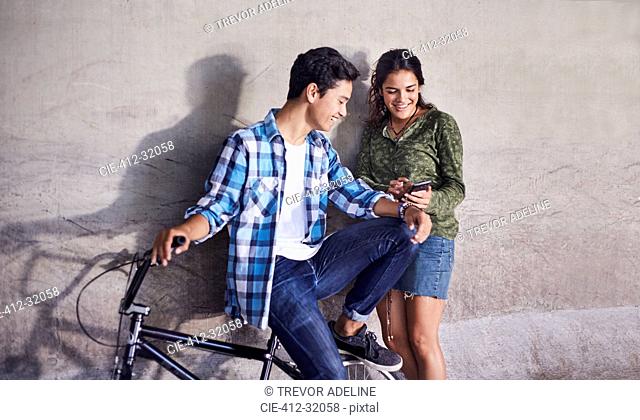 Teenage couple with BMX bicycle texting with cell phone at wall