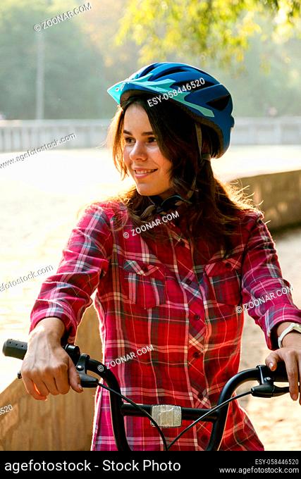 Subject ecological mode of transport bicycle. Beautiful young kasazy woman wearing a blue helmet and long hair poses standing next to an orange-colored rental...