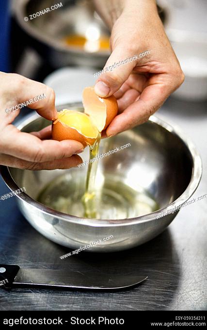 The chef breaks egg in a steel cup on professional kitchen