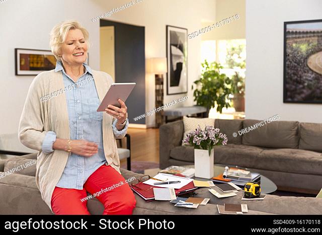 Mature Caucasian female designer working from home, sitting on back of couch with fabric swatches and notes laid out around her