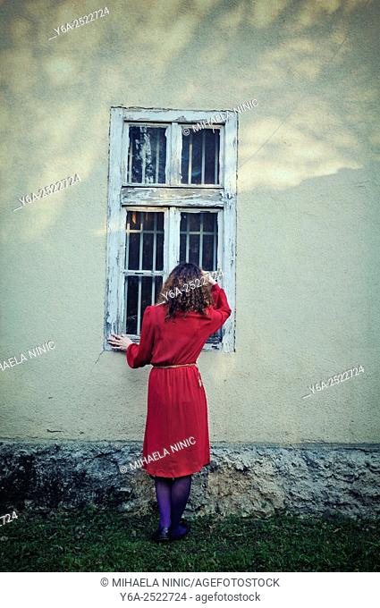 Woman standing outside the house looking through window