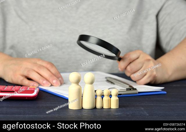 wooden figurines of little men family on the background of a man with a magnifying glass, who will examine the documents