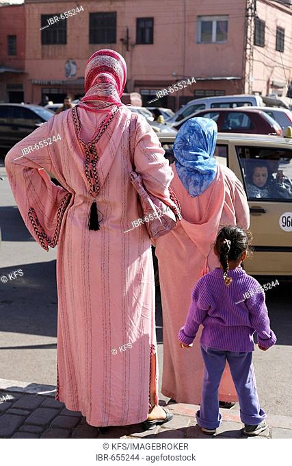 Two woman wearing pink djellabas and a little girl waiting by the roadside in the historic Medina quarter of Marrakesh, Morocco, Africa