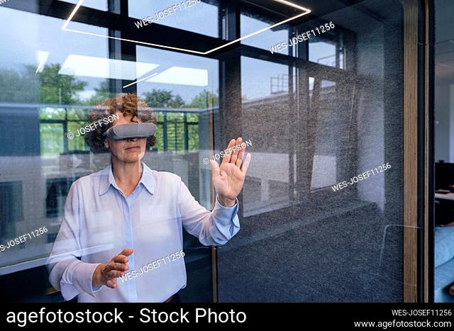 Businesswoman wearing virtual reality simulator gesturing seen through glass