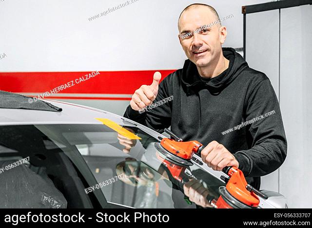 Automobile technician worker replacing windscreen or windshield of a car in auto service station garage. High quality photo