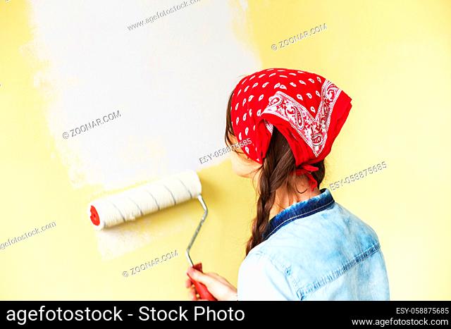Beautiful girl in red Headband painting the wall with paint roller. Portrait of a young beautiful woman painting wall in her new apartment