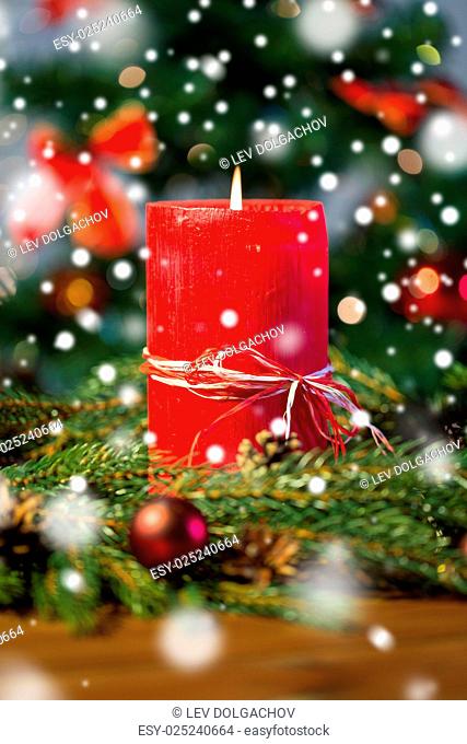 christmas, decoration, holidays and advertisement concept - close up of natural green fir branch wreath with red burning candle on wooden board