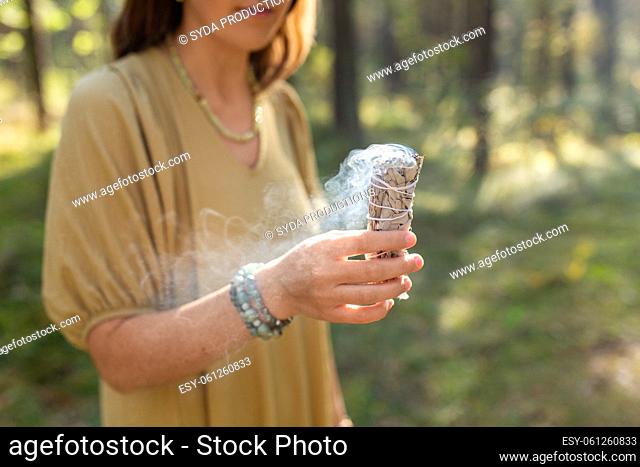 woman with sage performing magic ritual in forest