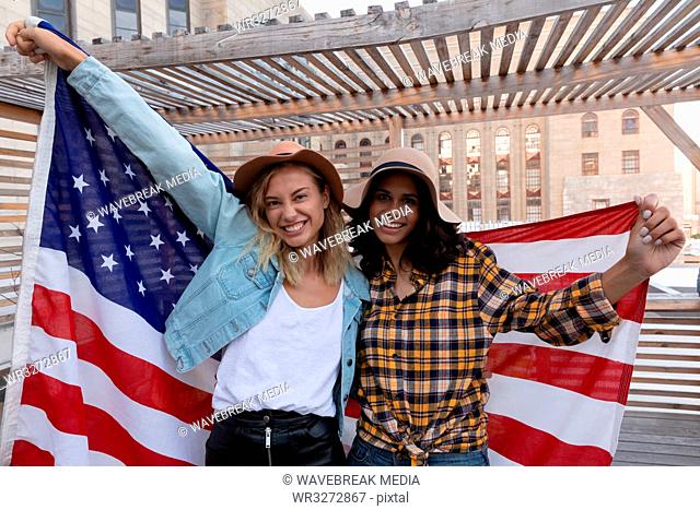 Female friends holding american flag in balcony at home