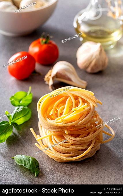 Italian pasta nest, basil, garlic and tomato. Uncooked spaghetti nest on kitchen table