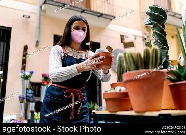Young female florist with protective face mask holding potted plant at store
