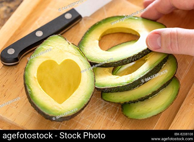 Male hand prepares fresh cut avocado with heart shaped pit area on wooden cutting board