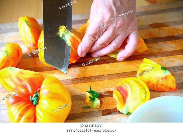 Yellow and orange-colored tomatoes with the hand of a man and a kitchen knife