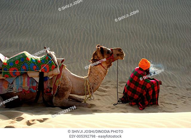 Man sitting with camel in sand dunes , Khuhri , Jaisalmer , Rajasthan , India