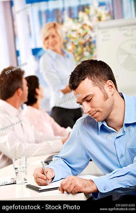 Young businessman sitting at table in office meeting room writing business notes
