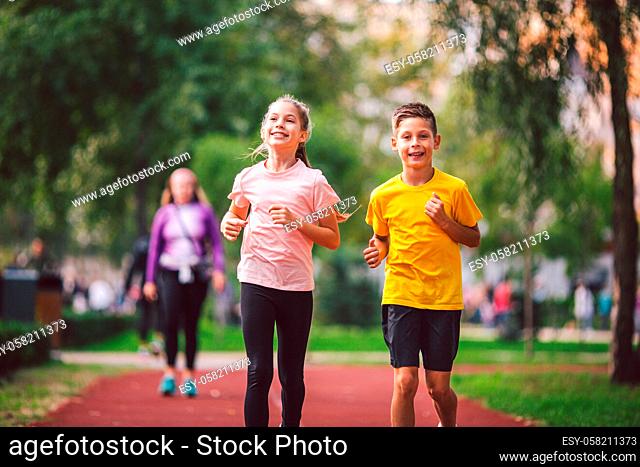 Sports and fitness in adolescence. Caucasian twins boy and girl run on the jogging track in the city park. Two children brother and sister for 10 years running...