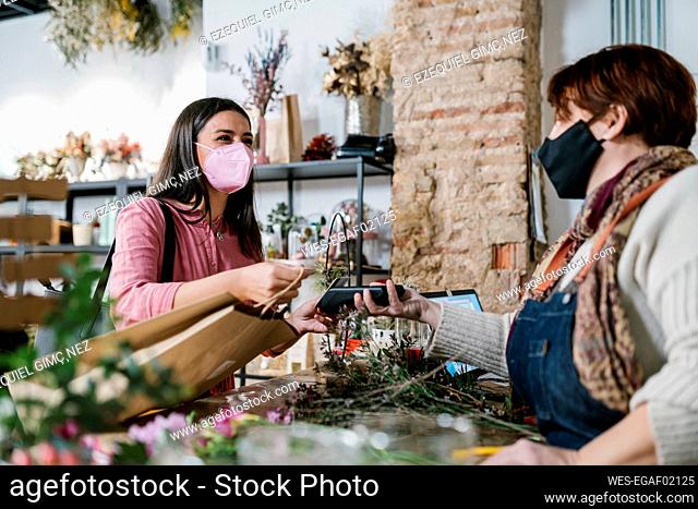Female customer paying through credit card to owner at flower shop