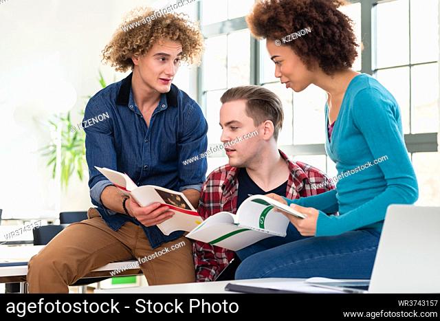 Three students sharing ideas and opinions while comparing information from two different textbooks during break at college