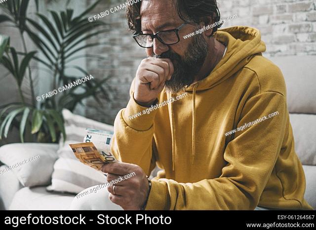 Man at home sitting on the sofa looking last money banknote to pay costs and bills family life. Worried people for job and economy problems