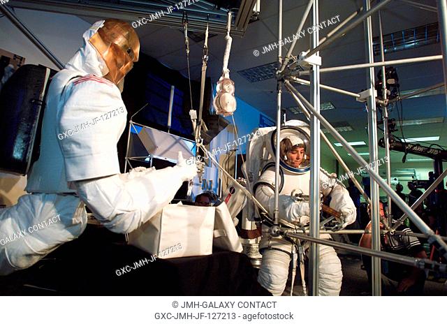 Astronaut Nancy J. Currie, wearing an advanced concept space suit, works on the assembly of an aluminum truss structure in cooperation with a non-human partner