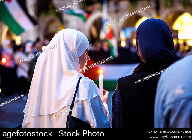 09 October 2023, Bavaria, Munich: A woman holds a candle in her hands during a rally for Palestine at Marienplatz, while a Palestinian flag can be seen in the...