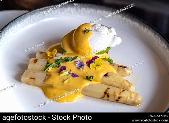 Gourmet grilled white asparagus with poached egg serve with hollandaise savory sauce decorate with edible colorful flowers