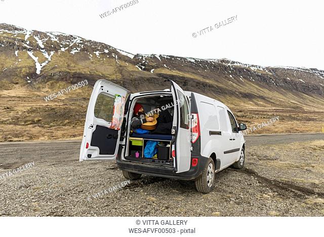 Iceland, man lying in van playing guitar