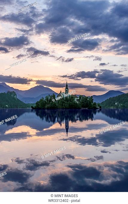 Village church and buildings reflected in still lake, Bled, Upper Carniola, Slovenia