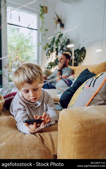 Boy using mobile phone while lying on sofa in living room