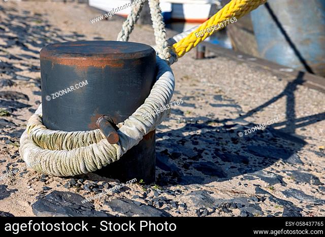 Detail steel bollard with tight ropes of moored ships