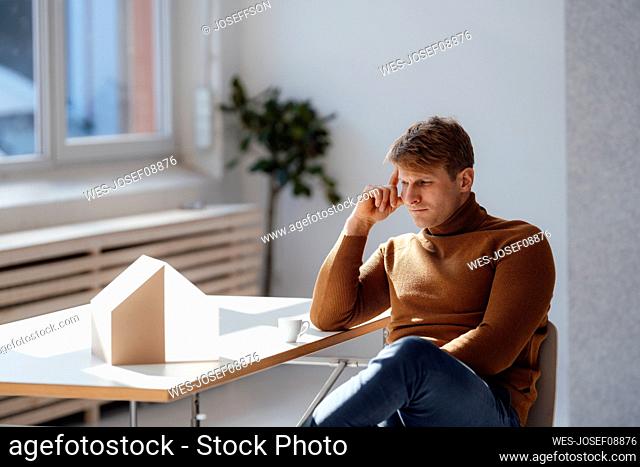 Thoughtful architect looking at model house in office