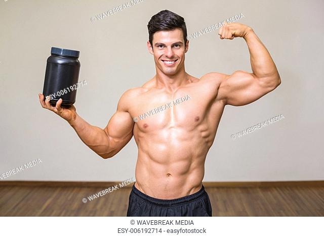 Muscular man posing with nutritional supplement in gym