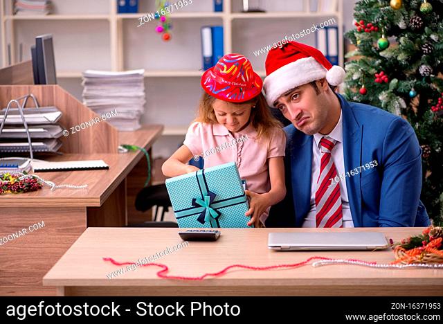 Young employee celebrating Christmas at workplace with his small daughter