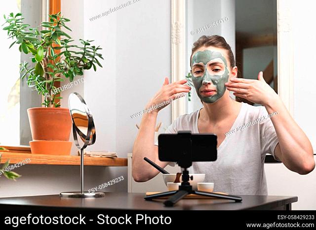 Beautiful white women making an online course of facial skin care and treatment with a green clay mask