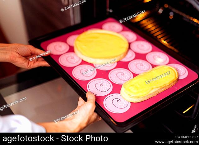 The confectioner puts the biscuit into the oven. On a red silicone sheet. Two forms