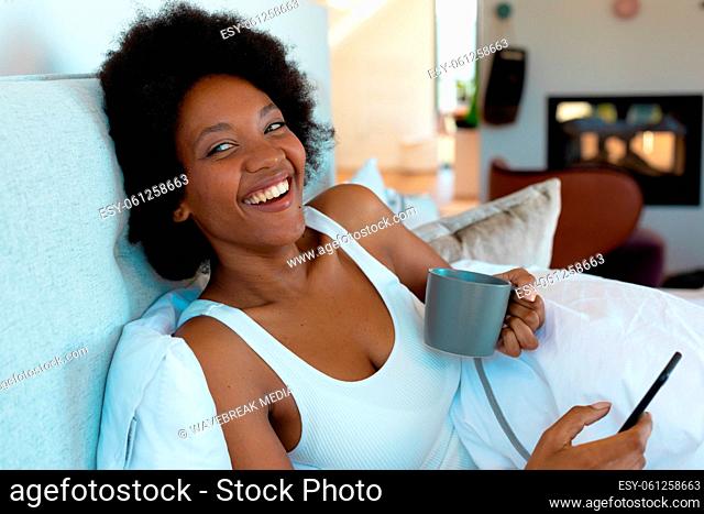 Cheerful young african american afro woman looking away while holding smart phone and coffee cup