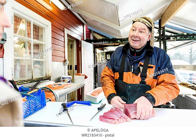 Smiling fisherman chopping fish while looking at female customer