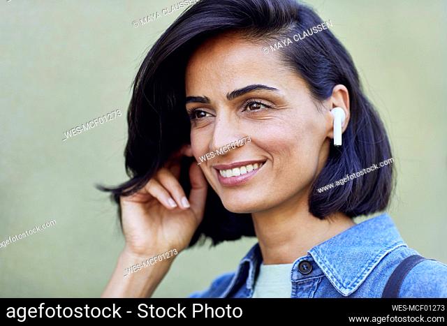 Close-up of smiling businesswoman wearing wireless headphones against wall