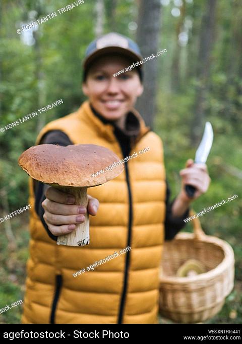 Smiling woman showing king bolete mushroom in forest