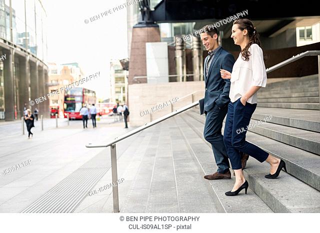 Rear view of young businessman and woman chatting whilst walking down stairway, London, UK