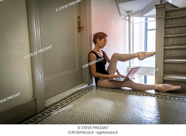 Ballerina using laptop beside staircase