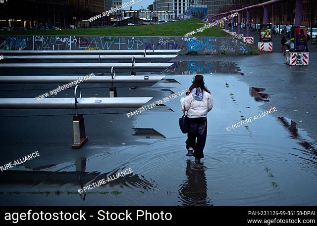19 November 2023, Berlin: 19.11.2023, Berlin. A girl with headphones walks through a large puddle about 100 meters from Potsdamer Platz in Tilla-Durieux-Park...