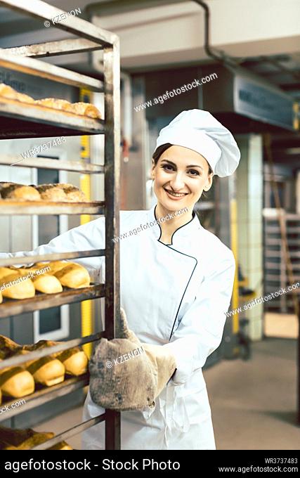 Baker woman pushing sheets with bread in the baking oven wearing bakers mittens