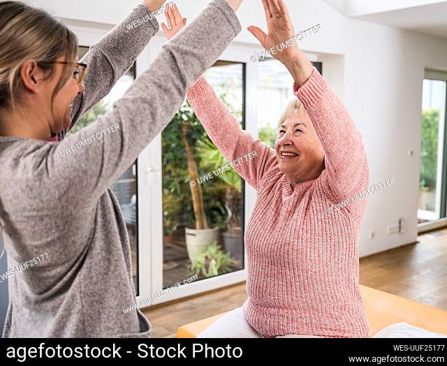 Young nurse cheering with senior woman at home