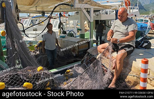 23 May 2021, Turkey, Antalya: The head of the fishing cooperative in Antalya, Cengiz Balta, stands on a boat while another cooperative member mends a net in the...