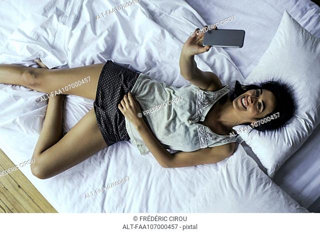Woman lying on bed taking selfie with smartphone