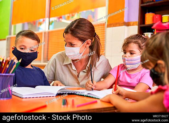 Lehrerin oder Tagesmutter gibt Nachhilfe in der Schule für Kinder mit Maske wegen Covid-19