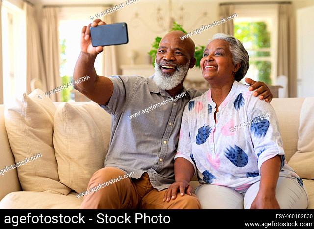 Senior african american couple sitting on sofa using smartphone taking selfies